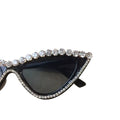 A pair of black sunglasses with a sparkling rhinestone frame, placed on a surface with a blurred background.