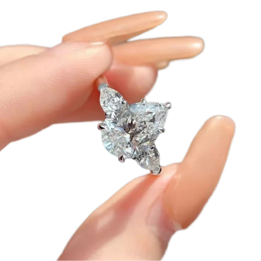 A close-up image of a person's hand holding a diamond ring with a large central diamond surrounded by smaller diamonds.
